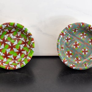 Puede incluir: Dos cuencos pequeños de cerámica con un patrón geométrico verde y rojo. Los cuencos están sobre una superficie negra.