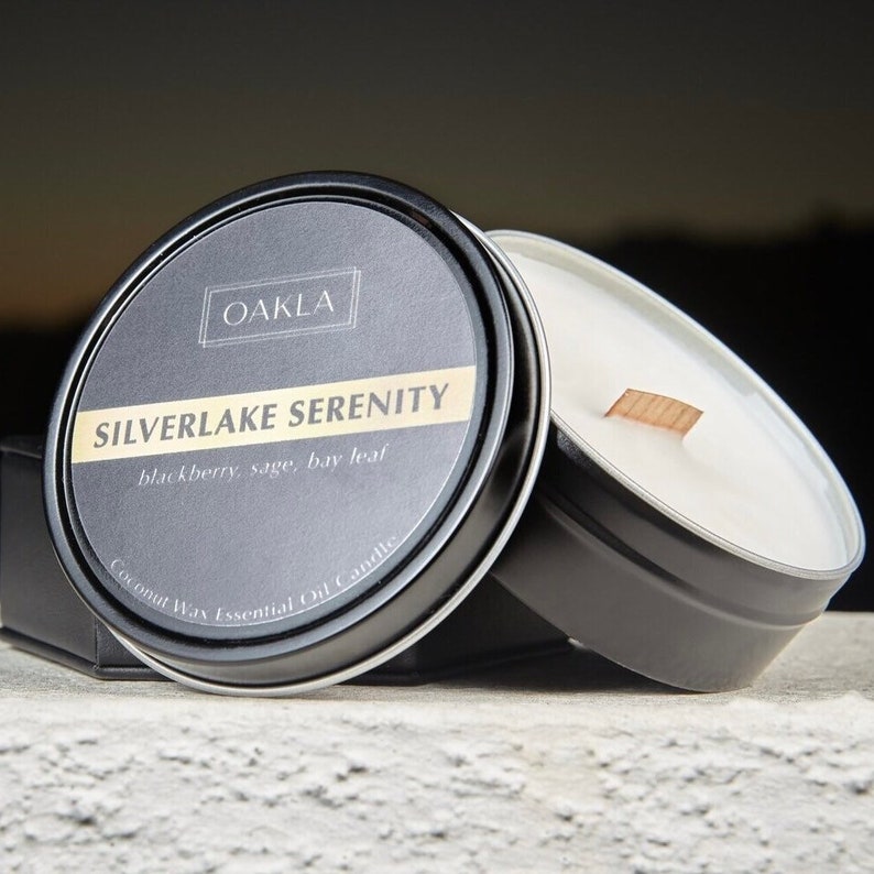May include: A black metal tin candle with a white label that reads "SILVERLAKE SERENITY blackberry sage, bay leaf Coconut Wax Essential Oil Candle" and a smaller label that reads "OAKLA".