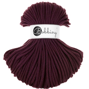 May include: A spool of deep burgundy cotton cord, wrapped in a spiral shape. The cord is labeled "Bobbiny" on a white tag.