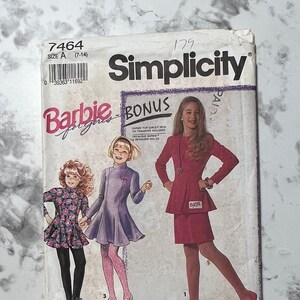 Peut inclure: Patron de couture Simplicity numéro 7464 pour robes de filles. Le patron comprend trois styles différents : une robe rose avec un basque, une robe violette avec une jupe évasée et une robe à imprimé floral avec un corsage ajusté et une jupe évasée. Le patron comprend également un transfert thermocollant bonus d'un logo Barbie.