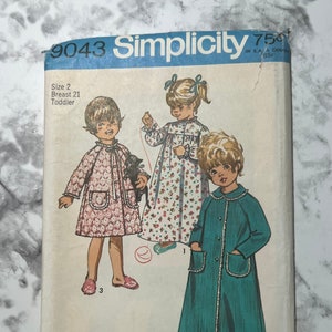 May include: Simplicity sewing pattern number 9043 for a toddler's robe. The pattern shows three different styles of robes, one in pink with white polka dots, one in teal blue, and one in white with pink flowers. The pattern is for sizes 2-4, with a 21-inch chest.