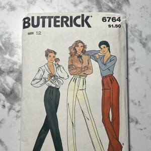 May include: A vintage Butterick sewing pattern, size 12, featuring illustrations of three women in different outfits. The outfits include blouses and high-waisted pants in various colors. The pattern number is 6764.
