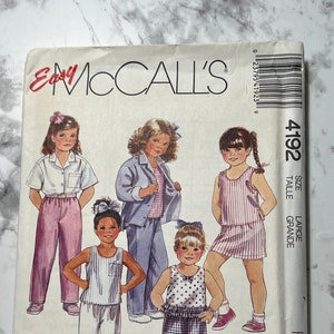 May include: A sewing pattern for children's clothing. The pattern is for a variety of styles, including a sleeveless dress, a shirt with shorts, a tank top with pants, and a jacket with pants. The pattern is from McCall's and is labeled "Easy Fashion Basics for Kids" and "Size Large/Taille Grande".