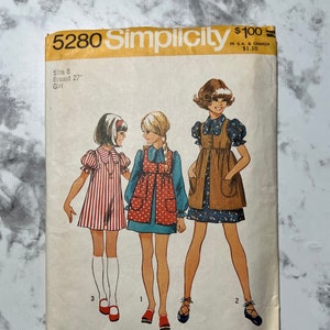 May include: Vintage Simplicity sewing pattern number 5280 for a girl's dress. The pattern is for size 8, with a 27 inch bust. The pattern shows three girls wearing different versions of the dress. The dress is a simple, A-line style with a Peter Pan collar and pockets. The pattern is printed on a white background with black text.