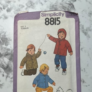May include: Vintage Simplicity pattern 8815 for toddler coats and pants. The pattern cover features illustrations of children in coats, pants, and a squirrel. The pattern is size 3, and the cover is purple and white.