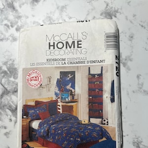 May include: A McCall's Home Decorating sewing pattern for a kids room. The pattern includes instructions for making a bedspread, pillowcases, and a wall organizer. The pattern features a blue and red color scheme with a cowboy theme.