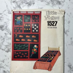 May include: A vintage Little Vogue sewing pattern, number 1527, for a children's quilt. The pattern features a red and black quilt with a variety of colorful appliques, including a clown, butterflies, stars, apples, whales, worms, and balloons.