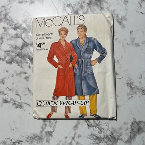 Puede incluir: Un patrón de costura McCall's para una bata de envoltura rápida. El patrón presenta una bata roja para una mujer y una bata azul para un hombre. El patrón está etiquetado como "Quick Wrap-Up" y tiene un valor de venta al público de $ 4.00.