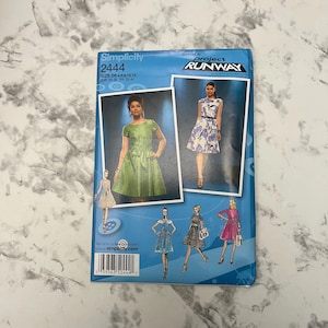 Könnte beinhalten: Ein Simplicity-Schnittmusterumschlag mit Kleiderillustrationen. Das blaue Cover zeigt "Simplicity 2444" und "Project Runway". Der Umschlag zeigt Kleiderdesigns in Grün, Blau und Rosa. Das Muster ist für die Größen 05, 06, 08, 10 und 12 sowie EUR-Größen 30-38.