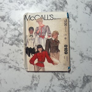 May include: A vintage McCall's sewing pattern packet featuring illustrations of women's blouses. The packet has the text "McCall's" and the number "8189". The illustrations depict various blouse styles with different designs and details.