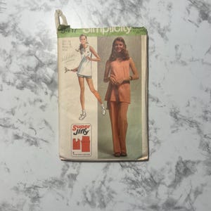 Könnte beinhalten: Vintage Simplicity Schnittmuster mit zwei Damenmode-Designs. Ein Design ist ein weißes Kleid mit blauem Besatz, das andere ein pfirsichfarbener Hosenanzug. Das Muster ist mit "Super Jiffy" gekennzeichnet und enthält Größenangaben.