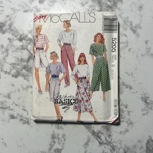 May include: A vintage McCall's sewing pattern envelope. The cover displays illustrations of women in different outfits, such as shorts, trousers, and skirts. The text "Fashion Basics" is visible, along with the pattern number 5205 and size information.