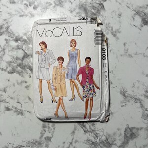 May include: A vintage McCall's sewing pattern packet featuring illustrations of women's clothing designs. The packet includes the number 8103 and size E (14, 16, 18). The front of the packet displays a variety of outfits, including dresses and suits.