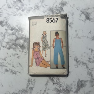 May include: A vintage Simplicity sewing pattern packet, number 8567, featuring illustrations of three different jumpsuit and romper designs. The packet is off-white with the pattern number in large, bold numbers.