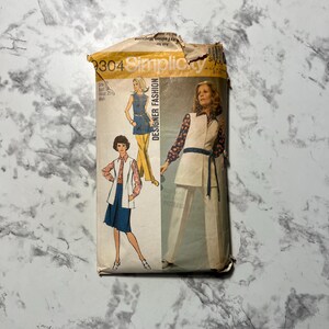 May include: A vintage Simplicity Designer Fashion sewing pattern. The pattern features illustrations of women's clothing designs, including a tunic, pants, and a skirt. The pattern envelope is beige and has the number 9304 printed on it.