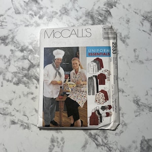 May include: A McCall's sewing pattern for a uniform, featuring a chef's coat, trousers, apron, and shirt. The pattern is for sizes 38-40, medium. The pattern is called "Uniform Essentials" and the pattern number is 2233.