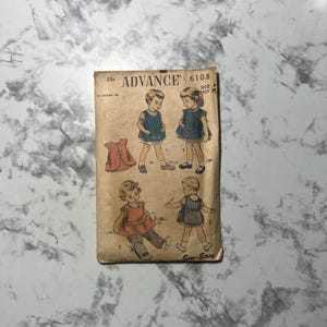May include: Vintage sewing pattern envelope for children's clothing. The pattern is for a dress and shorts, and the envelope features illustrations of children wearing the garments. The pattern number is 6108, and the size is 6, with a 24-inch breast measurement. The pattern is from Advance, and the text "Sew-Easy" is printed on the bottom.