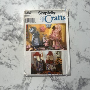 Puede incluir: Patrón de costura Simplicity Crafts número 8387 para hacer muñecas. El patrón incluye instrucciones para hacer una muñeca con un vestido de cuadros, una muñeca con un vestido rosa y dos muñecas conejitas. El patrón es de Faith Van Zanten.