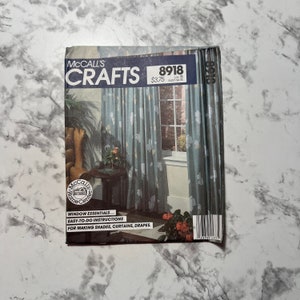 Puede incluir: Un paquete de patrones McCall's Crafts vintage. La portada presenta un diseño de cortinas color turquesa con detalles florales blancos. El paquete incluye instrucciones para hacer cortinas, visillos y cortinajes. El número de patrón es 8918.