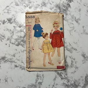 May include: Vintage Simplicity sewing pattern number 5553 for a child's dress. The pattern is printed in Canada and includes three different dress styles. The dresses are shown on three young girls wearing the dresses in different colors and patterns.