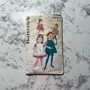 May include: Vintage sewing pattern for a girl's dress with a Peter Pan collar and pockets. The pattern is from Butterick and is number 9888. The pattern is for sizes 23 1/2 to 32.
