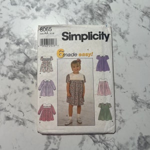 May include: Simplicity sewing pattern number 8065 for girls' dresses. The pattern includes six different styles of dresses, all with a Peter Pan collar and a gathered skirt. The pattern is for sizes AA, 1, and 2.