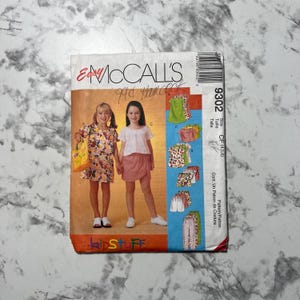 以下が含まれることがあります： 子供服のヴィンテージMcCall'sソーイングパターン。パターンには、衣服を着ている2人の若い女の子のイラストが掲載されています。パターンには、さまざまなトップス、スカート、ショーツが含まれています。パターン番号は9302です。