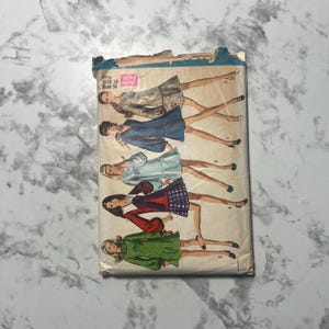 May include: Vintage sewing pattern featuring illustrations of women in various dresses. The pattern is labeled "Miss Size 12 Bust 34" and includes a "New Sizing" sticker. The cover shows a variety of dress styles in different colors and patterns.