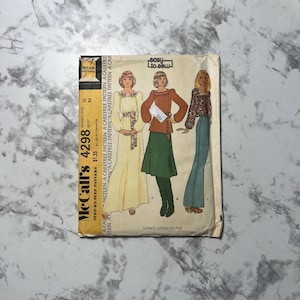 May include: Vintage McCall's sewing pattern number 4298 for a misses' dress or top. The pattern includes three different styles: a long, flowing dress with a gathered neckline, a shorter dress with a gathered neckline and a belt, and a top with a gathered neckline and long sleeves. The pattern is printed on a white background with black text and illustrations.
