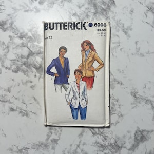 May include: Vintage Butterick sewing pattern 6998 featuring illustrations of blazers. The pattern shows three different blazer styles in various colors, including blue, tan, and white. The pattern is for size 12.