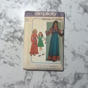 May include: Simplicity sewing pattern number 7778 for girls sizes 7 and 8. The pattern is for a personal fit dress with a long skirt and a bib style top. The pattern cover shows three girls wearing the dress in different colors and styles.