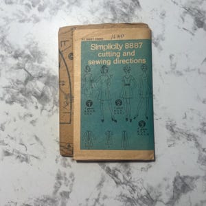 May include: A vintage Simplicity 8887 sewing pattern. The front cover is teal with illustrations of dresses and the text "Simplicity 8887 cutting and sewing directions." The pattern includes diagrams and instructions for various dress styles.
