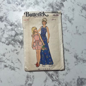May include: A vintage sewing pattern for girls' dresses. The pattern is for sizes 7-14 and features two girls wearing the dresses. The dress on the left is red and white striped with a white apron and pockets. The dress on the right is blue with a floral print. The pattern is from Butterick, The Fashion One, and is number 3691.