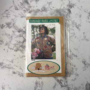 May include: A sewing pattern for a jacket called "Thready Bare Jacket" from The Thread Bare Pattern Company. The pattern features a woman wearing a brown jacket with colorful patchwork details. The pattern number is TBJ-96.