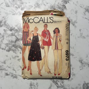 以下が含まれることがあります： 女性用衣料デザインのイラストが描かれた、ヴィンテージMcCall'sの裁縫パターン封筒。「McCall's」の文字と価格が記載されています。パターン番号は6973で、バストサイズは91cmです。