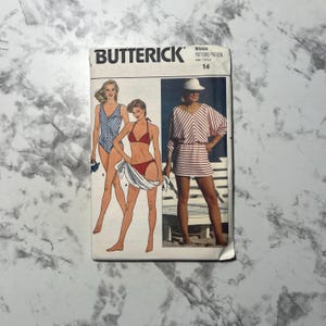 May include: A vintage Butterick sewing pattern featuring illustrations of swimwear designs. The cover displays three women in different swimsuits, including a striped one-piece, a bikini, and a striped tunic. The pattern number is 6555, size 14.
