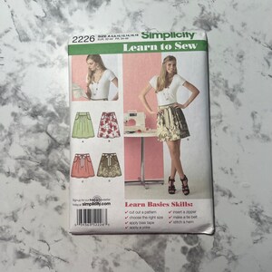 May include: Simplicity sewing pattern number 2226, Learn to Sew, for sizes 6-18. The pattern includes instructions for making a skirt with a tie belt. The pattern cover features a model wearing a white top and a floral skirt. The pattern also includes basic sewing skills.