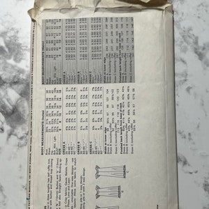 May include: A sewing pattern for a loose-fitting dress with a self ruffle trim. The pattern includes three different dress lengths and a chart with measurements for each size. The pattern is for sizes 6-16.