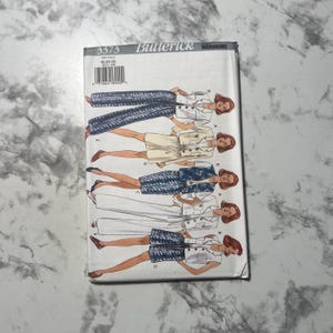 May include: A Butterick Wardrobe sewing pattern packet, featuring illustrations of various women's clothing designs. The packet includes a variety of outfits, including pantsuits, skirts, and jackets. The pattern number is 3373, and the size range is 18-20-22.