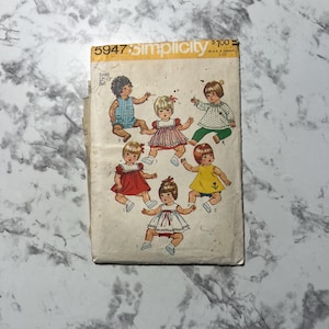 May include: Vintage Simplicity sewing pattern for small 30-33 cm dolls. The pattern envelope features illustrations of dolls in various outfits. The envelope is yellowed with age and has the number 5947 printed on it.