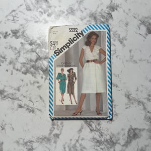 May include: Simplicity sewing pattern number 5532 for a dress with a wrap style and a collar. The pattern is for sizes 12 to 22. The pattern is by Cathy Hardwick.