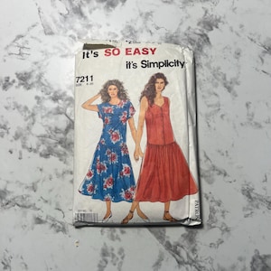 May include: A vintage sewing pattern titled "It's So Easy, it's Simplicity." The pattern features illustrations of two dresses: one blue with a floral print and the other a solid red dress. The pattern number is 7211, size 8-20.