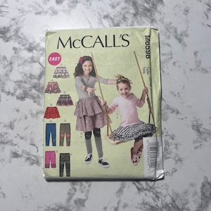 May include: A sewing pattern for girls' clothing, featuring a tiered skirt and leggings. The pattern is labeled "McCall's Easy" and includes instructions for making different styles of skirts and leggings.