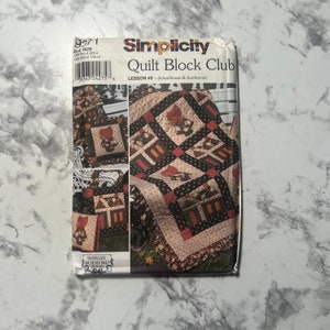 May include: A Simplicity Quilt Block Club pattern for lesson #5, featuring a schoolhouse and sunbonnet design. The pattern includes a quilt block with a red, black, and white color scheme.