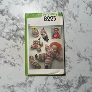 May include: Simplicity sewing pattern number 8225 for making stuffed toys. The pattern includes instructions for making a clown, a caterpillar, a dachshund, an owl, and a rag doll. The toys are all made with colorful fabric and have a whimsical look.