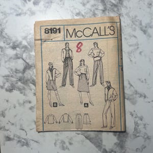 以下が含まれることがあります： さまざまな衣装のイラストが特徴の、ヴィンテージMcCall'sの裁縫パターン。 パターン番号は8191で、手書きの赤い数字8が付いています。 カバーはベージュで、青と黒のテキストとイラストが描かれています。