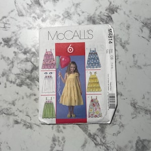 May include: A McCall's sewing pattern for a girl's dress. The pattern includes six different styles of dresses, all with a tiered skirt. The pattern is for sizes 1-2-3. The pattern number is M4814.