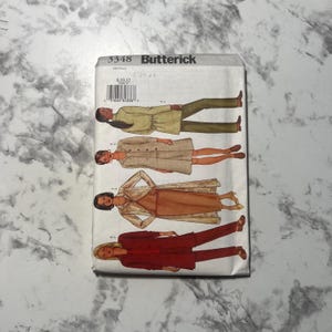 May include: A vintage Butterick sewing pattern envelope with illustrations of four outfits. The outfits include a green jacket and trousers, a beige coat, a patterned coat and dress, and a red suit. The envelope has the number 3348 printed on it.