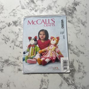 May include: McCall's Crafts sewing pattern for making two plush toys, a cat and a dog. The pattern is for size OSZ and is number M6980. The pattern features a young girl holding the two toys.