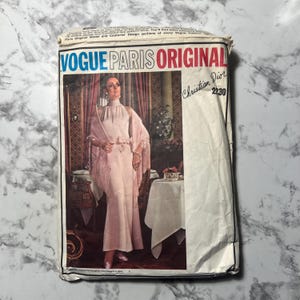 Könnte beinhalten: Ein Vintage-Schnittmuster von Vogue Paris Original mit einem Christian Dior-Design. Die Schnittmusterpackung zeigt eine Frau in einem rosa Kleid und Schal. Der Text "VOGUE PARIS ORIGINAL" ist deutlich sichtbar.